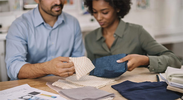 Two professionals collaborating with fabric swatches at table, coordinating with suppliers to develop production-feasible textile samples